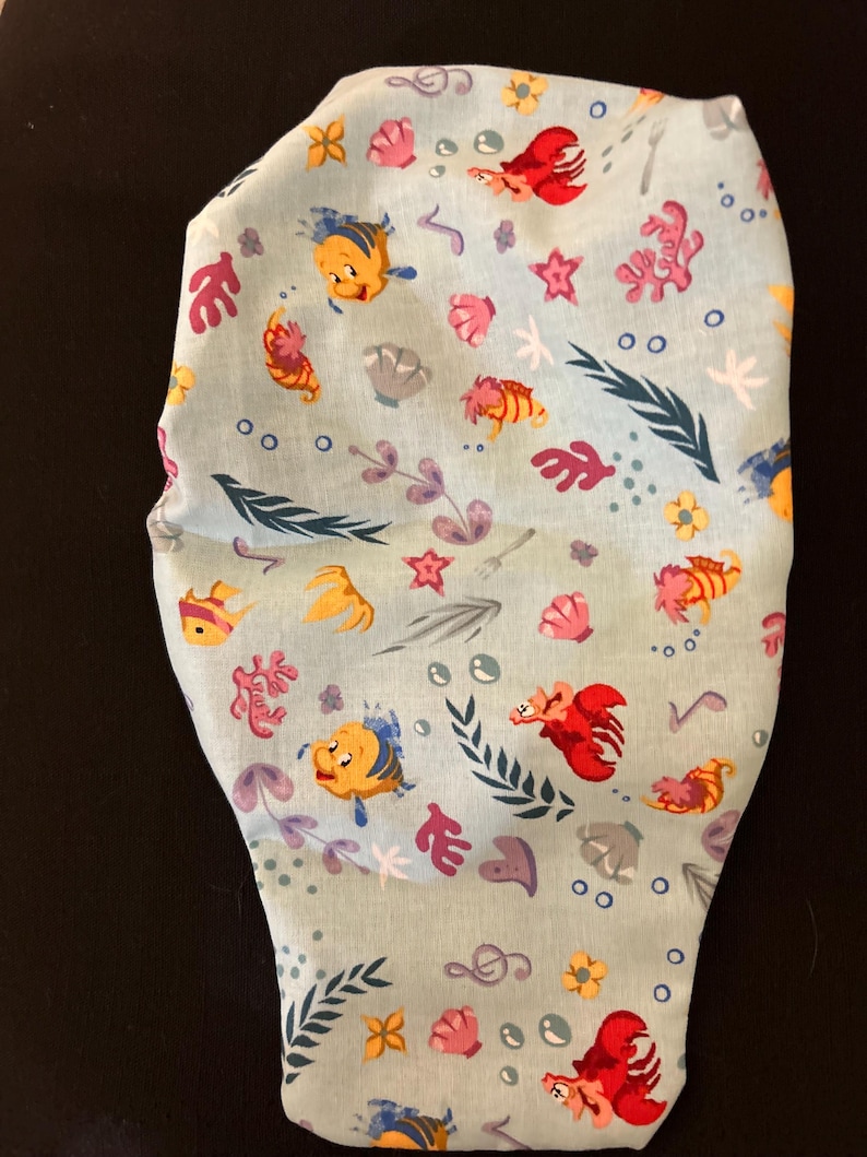 K&ouml;nnte beinhalten: Ein hellblauer Stoff mit einem sich wiederholenden Muster aus gelben und orangefarbenen Fischen, roten Hummern, rosa Muscheln und gr&uuml;nem Seetang. Der Stoff ist perfekt f&uuml;r Bastelprojekte wie Gesichtsmasken.