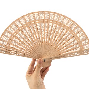 K&ouml;nnte beinhalten: Ein hellbrauner F&auml;cher aus Holz mit einem filigranen, komplizierten Design. Der F&auml;cher ist geschlossen und tr&auml;gt eine personalisierte Inschrift mit dem Text "Sophia & Michael 02.20.2023".