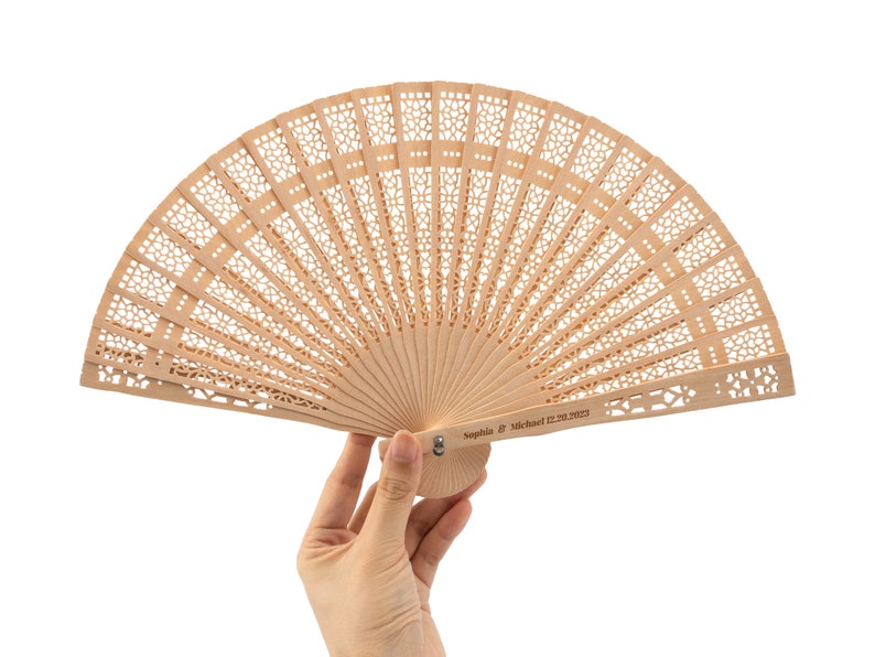 K&ouml;nnte beinhalten: Ein hellbrauner F&auml;cher aus Holz mit einem filigranen, komplizierten Design. Der F&auml;cher ist geschlossen und tr&auml;gt eine personalisierte Inschrift mit dem Text "Sophia & Michael 02.20.2023".