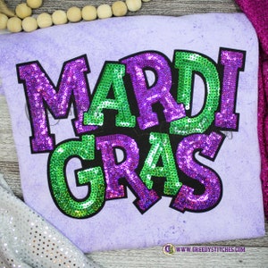 May include: Purple and green sequined Mardi Gras shirt with the text "Mardi Gras" on a light purple background.