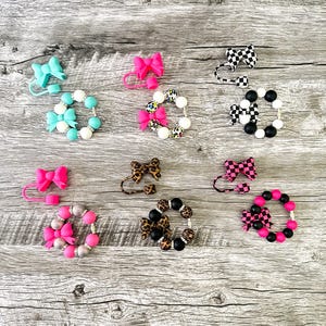 May include: A collection of baby pacifier clips and matching beaded bracelets. The clips feature bows in various colors and patterns, including pink, turquoise, and leopard print. The bracelets have coordinating beads.