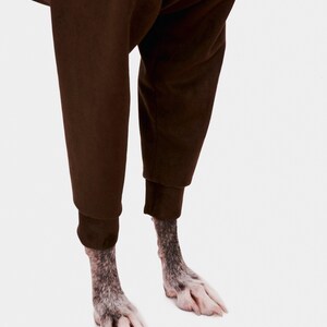 May include: A pair of brown trousers with the legs rolled up to reveal the paws of a dog.
