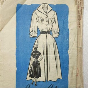 May include: A vintage sewing pattern for a white dress with a collar, buttons, and a belt. The dress has a full skirt and three-quarter sleeves. The pattern is illustrated with a woman wearing the dress.