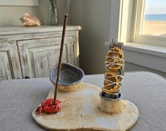 May include: A ceramic tray with a speckled cream finish featuring a small red crab sculpture holding an incense stick, a small bowl, and a cylindrical holder containing a bundle of dried herbs wrapped with twine and two dried orange slices.