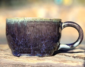 May include: A dark blue and green ceramic mug with a textured glaze. The mug has a rounded shape and a handle.