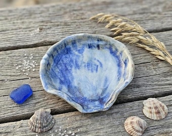 May include: A shell-shaped ceramic dish featuring a glossy glaze with blended shades of deep blue and white. The dish has an irregular, organic rim and a smooth, concave interior surface, showcasing a handcrafted appearance and coastal aesthetic.