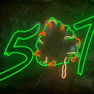 May include: Neon sign with the number 507 in green, with a large orange and white circular design in the center.