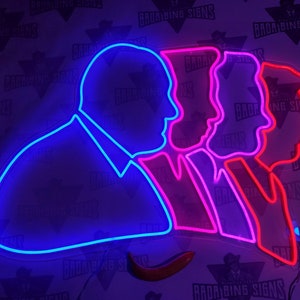 May include: Neon sign depicting three profile silhouettes of people. The leftmost silhouette is blue, the middle silhouette is pink, and the rightmost silhouette is red. The silhouettes are all facing the right side of the image.