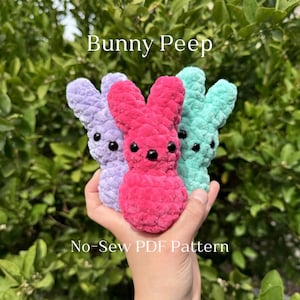 May include: Three plush bunny peep toys in pink, purple and teal colours. The toys are made of fuzzy yarn and have black eyes. The text "Bunny Peep No-Sew PDF Pattern" is displayed below the toys.