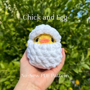 May include: A white crocheted chick peeking out of an egg with the text "Chick and Egg No-Sew PDF Pattern"