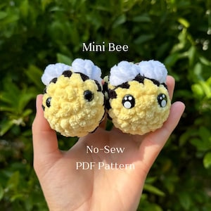 May include: Two small crocheted bee plushies with black and yellow stripes, white wings, and black eyes. The plushies are held in a hand and the text "Mini Bee No-Sew PDF Pattern" is below them.