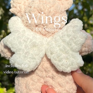 May include: A plush, pink and white angel wings pattern. The text "Wings PDF Pattern" is displayed in white. The description also includes the text "Includes full video tutorial!"