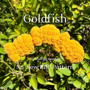 May include: A crochet pattern for a goldfish, with the text "Goldfish No-Sew PDF Pattern" and "No stuffing needed".