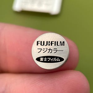 May include: A silver battery with the text "FUJIFILM" in black, followed by "フジカラー" in Japanese, and "富士フィルム" in Japanese.