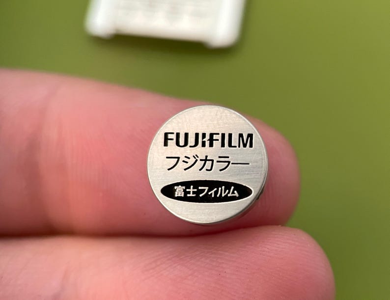 May include: A silver battery with the text "FUJIFILM" in black, followed by "フジカラー" in Japanese, and "富士フィルム" in Japanese.