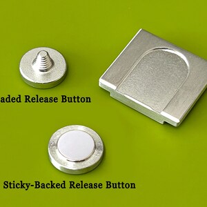 K&ouml;nnte beinhalten: Silberfarbene Hardware-Komponenten auf gr&uuml;nem Hintergrund. Das Bild zeigt einen Gewinde-Entriegelungsknopf, einen selbstklebenden Entriegelungsknopf und ein rechteckiges Teil. Der Text auf dem Bild lautet "Threaded Release Button" und "Sticky-Backed Release Button."