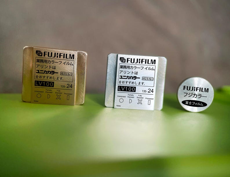May include: Three gold and silver metal film canisters with the text "FUJIFILM" and "ユニカカラー" printed on them. The canisters are labeled "LV100" and "135-24".