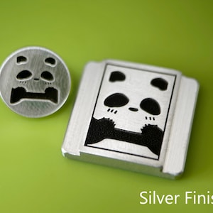 May include: Two silver-toned metal panda-themed items on a green background. One is a round button with a panda face, the other is a rectangular shape with a panda face. The text "Silver Finish" is at the bottom.