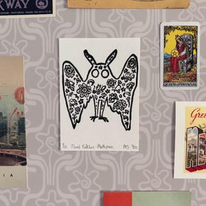 Può includere: Illustrazione in bianco e nero di una falena con motivi floreali sulle ali. L'opera d'arte è su una carta bianca, con il testo "1/2 Floral Folklore-Mothman MS 'bs". Altre cartoline e opere d'arte vintage sono sullo sfondo.
