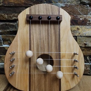 May include: A wooden musical instrument with strings and wooden balls that hang from the strings. The instrument is made of cherry and walnut wood and has a natural finish.