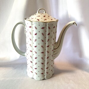 May include: White porcelain coffee pot with a gold trim and a floral pattern. The pot has a tall, slender body and a curved spout.