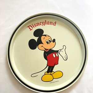 May include: A white metal serving tray with a black rim. The tray features a cartoon image of Mickey Mouse in the center, with the text "Disneyland" above him. The copyright text "&copy; Walt Disney Productions" is at the bottom of the tray.