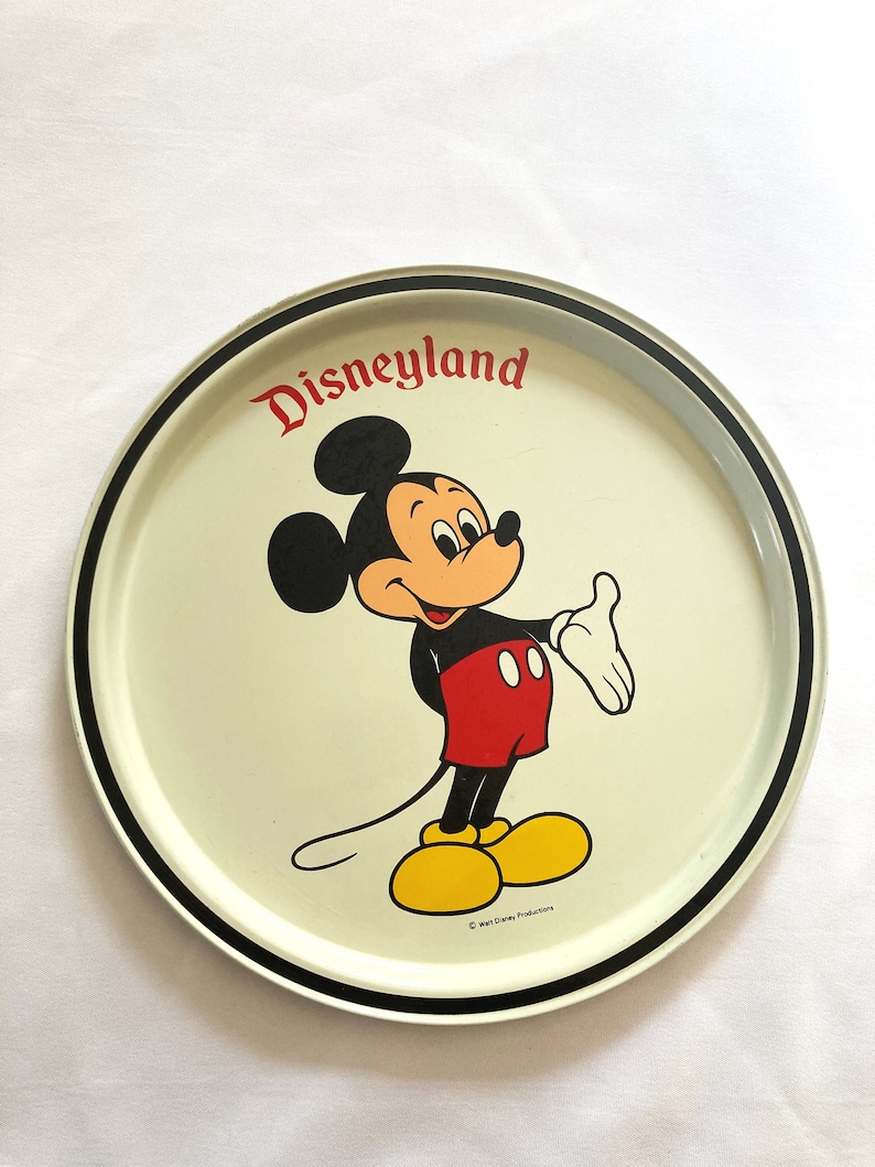 May include: A white metal serving tray with a black rim. The tray features a cartoon image of Mickey Mouse in the center, with the text "Disneyland" above him. The copyright text "&copy; Walt Disney Productions" is at the bottom of the tray.