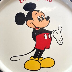 May include: White metal tray with a black border. The center of the tray features a cartoon image of Mickey Mouse in color. The text "Disneyland" is printed in black at the top of the tray. The text "&copy; Walt Disney Productions" is printed in black at the bottom of the tray.