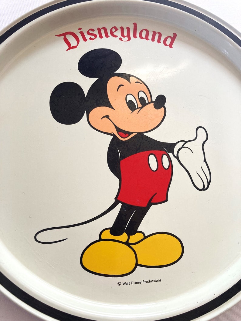 May include: White metal tray with a black border. The center of the tray features a cartoon image of Mickey Mouse in color. The text "Disneyland" is printed in black at the top of the tray. The text "&copy; Walt Disney Productions" is printed in black at the bottom of the tray.