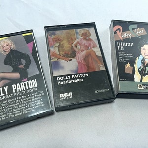 May include: Three cassette tapes featuring country music artists Dolly Parton and Patsy Cline. The tapes are black with clear plastic windows showing the album covers. The Dolly Parton tapes are titled "The Great Pretender" and "Heartbreaker". The Patsy Cline tape is titled "10 Greatest Hits".