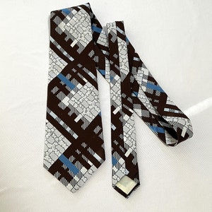 May include: A brown, blue, and white patterned tie with a geometric design. The tie is made of a silky fabric and has a pointed tip.