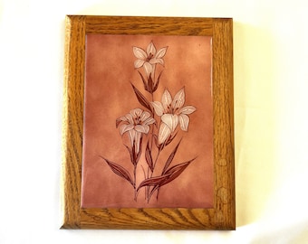 May include: A framed floral art piece featuring a stylized lily design. The artwork has a light brown background with white and brown lilies. The frame is made of light brown wood.