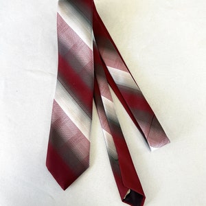 May include: A burgundy and gray striped necktie. The tie features diagonal stripes in shades of burgundy, gray, and white. The tie is made of a smooth fabric and is displayed on a white background.