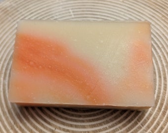 May include: A rectangular bar of soap with a swirl of orange and white. The soap is on a wooden surface.