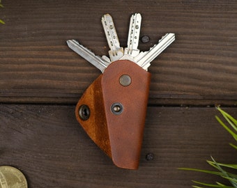 May include: A brown leather key holder with a flap closure and a set of keys inside. The key holder has a distressed look and is made of genuine leather.