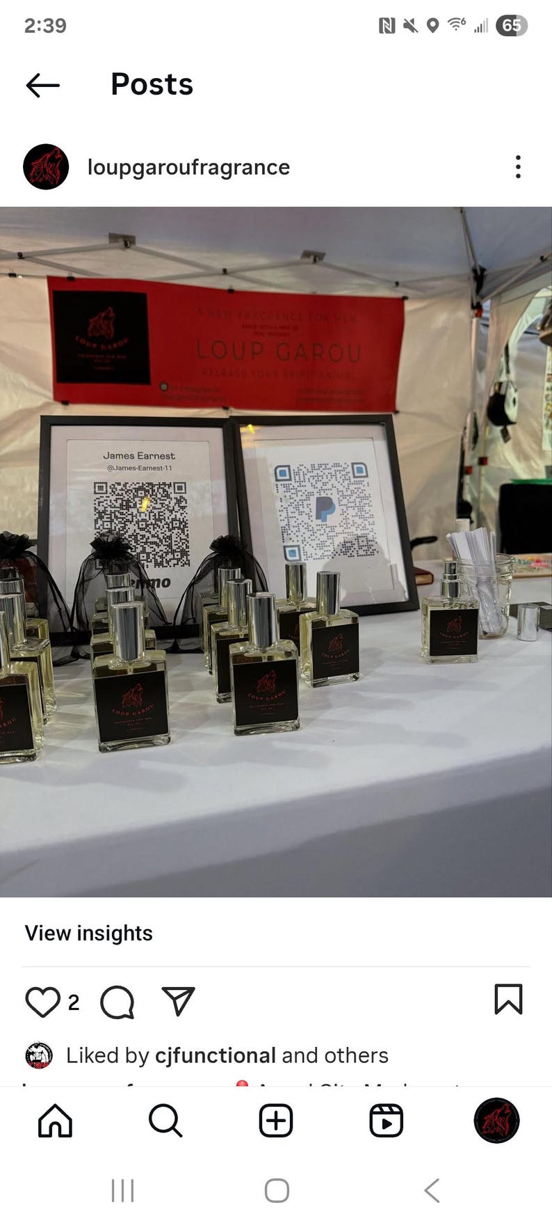 May include: A display of perfume bottles with black labels and silver caps. The bottles are arranged on a white table, with framed QR codes and a red banner that reads "LOUP GAROU". The brand name and a wolf logo are visible.