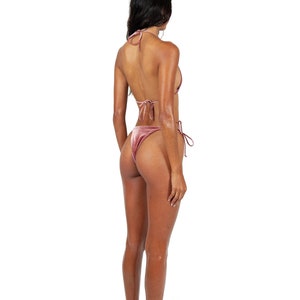 May include: A woman wearing a pink velvet bikini. The bikini top is a triangle style with thin straps. The bikini bottom is a high-cut style with ties on the sides.