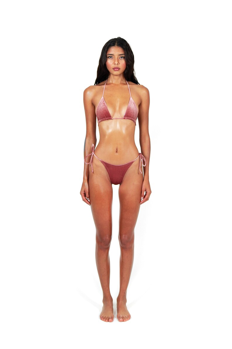 May include: A woman wearing a dusty rose velvet bikini top and matching bikini bottom. The bikini top is a triangle style with thin straps. The bikini bottom is a tie-side style.