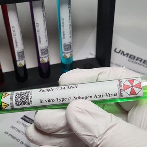 Puede incluir: Un tubo de ensayo de vidrio transparente con una tapa negra, lleno de líquido verde, etiquetado como "In vitro Type // Pathogen Anti-Virus". El tubo es sostenido por una mano enguantada, con otros tubos de ensayo en un soporte negro en el fondo. El logotipo de Umbrella Corporation es visible.