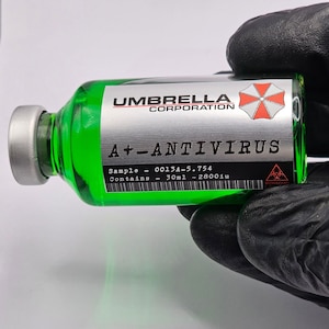 Könnte beinhalten: Eine grüne Glasampulle mit der Aufschrift "A+ - ANTIVIRUS" und dem Logo der Umbrella Corporation. Die Ampulle enthält 30 ml Flüssigkeit und wird von einer behandschuhten Hand gehalten. Das Etikett enthält ein Biohazard-Symbol.