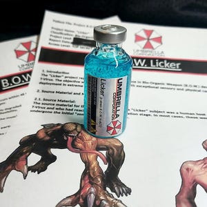 Peut inclure: Un petit flacon en verre rempli d'un liquide bleu vif, doté d'un bouchon argenté et d'une étiquette indiquant Umbrella Corporation Licker, posé sur un document illustré d'une créature et du logo de l'Umbrella Corporation.