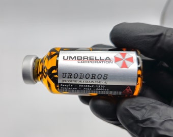 Peut inclure: Fiole en verre avec un bouchon et une étiquette argentés, remplie d'un liquide orange. L'étiquette indique "UMBRELLA CORPORATION" et "UROBOROS". La fiole contient 30 ml de liquide. Le fond est gris clair.