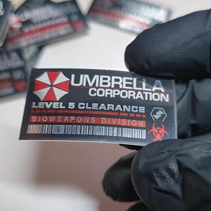 Adesivo Resident Evil Bioweapons Division Umbrella Corporation 45 mm X 25 mm Etichetta autoadesiva argentata Stampa UV di alta qualità