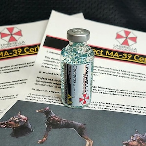 Może przedstawiać: Przezroczysta szklana fiolka wypełniona niebieskim brokatem, zamknięta srebrną nakrętką. Etykieta zawiera napis Umbrella Corporation Cerberus B.O.W. MA-39. Fiolka stoi na dokumentach zatytułowanych Project MA-39 Cerberus z logo Umbrella Corporation.