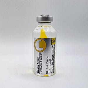 Op de afbeelding: Een doorzichtig glazen flesje met een zilveren metalen dop met daarin een felgele kristal. Het etiket bevat de tekst Black Mesa Research Facility, Dr. Eli Vance, Gamma Labs en Sample: Xen Crystal GG-3883 met een stralingswaarschuwingssymbool.