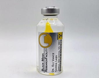 May include: A clear glass vial with a silver metal cap containing a bright yellow crystal. The label features the text Black Mesa Research Facility, Dr. Eli Vance, Gamma Labs, and Sample: Xen Crystal GG-3883 with a radiation warning symbol.