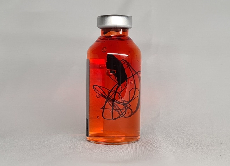 May include: A clear glass bottle with a silver cap, filled with a vibrant orange liquid. The bottle features a black abstract design. The bottle is likely for essential oils or a similar product.