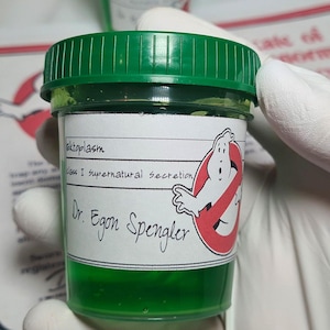 May include: A small, clear jar with a green lid and a label featuring the Ghostbusters logo. The label reads "Ectoplasm, Class I Supernatural Secretion, Dr. Egon Spengler." The jar is filled with a vibrant green liquid.
