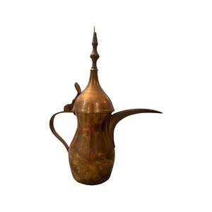 May include: A vintage brass coffee pot with a long spout, curved handle, and ornate lid. The pot has etched floral and geometric patterns. The pot is a warm, golden color and is set against a white background.