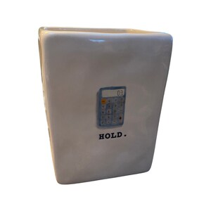 May include: White ceramic container with a calculator graphic and the word "HOLD." The calculator displays "03" on its screen. The container has a rectangular shape with slightly angled sides.